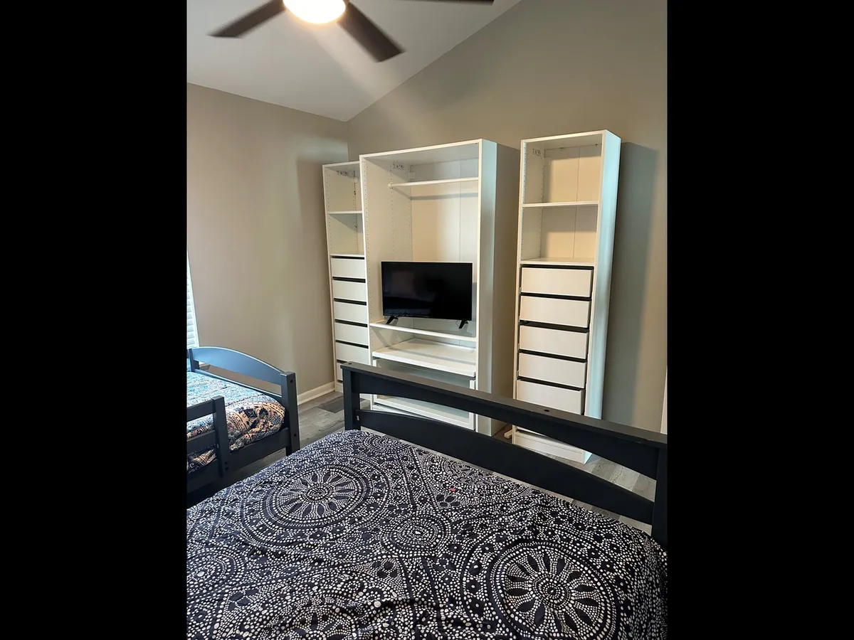 This image captures a well-organized bedroom with a bed adorned in decorative bedding, accessible storage units, and a television mounted at a comfortable viewing height. The space looks tidy and comfortable, ideal for relaxation or entertainment.