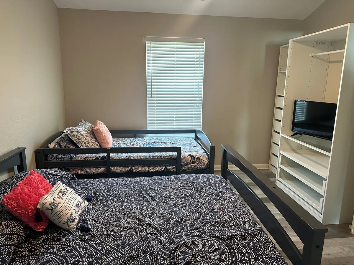 This image shows a cozy bedroom featuring a set of bunk beds with decorative pillows and a television unit nearby. The Twin over Full bunk design is practical for families with children, offering both comfort and versatility. The space feels inviting and relaxed, with soft lighting and thoughtful decor.