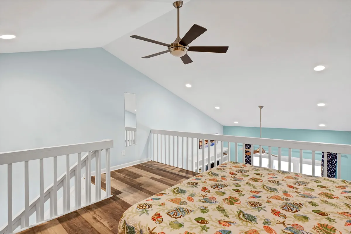 This image highlights an upper-level sleeping area with a colorful bedspread, wooden flooring, and a view of the loft railing, creating an open and airy feel. The space is bright with natural light, evoking a cheerful and inviting mood—ideal for couples or friends seeking separation and comfort.