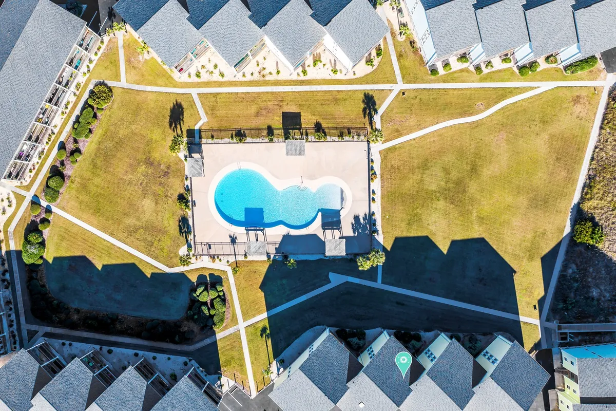 An exterior image showcasing a sparkling swimming pool surrounded by grassy areas, walkways, and adjacent condo buildings. The scene hints at both leisure and activity, with ample outdoor space for breaks between work sessions.