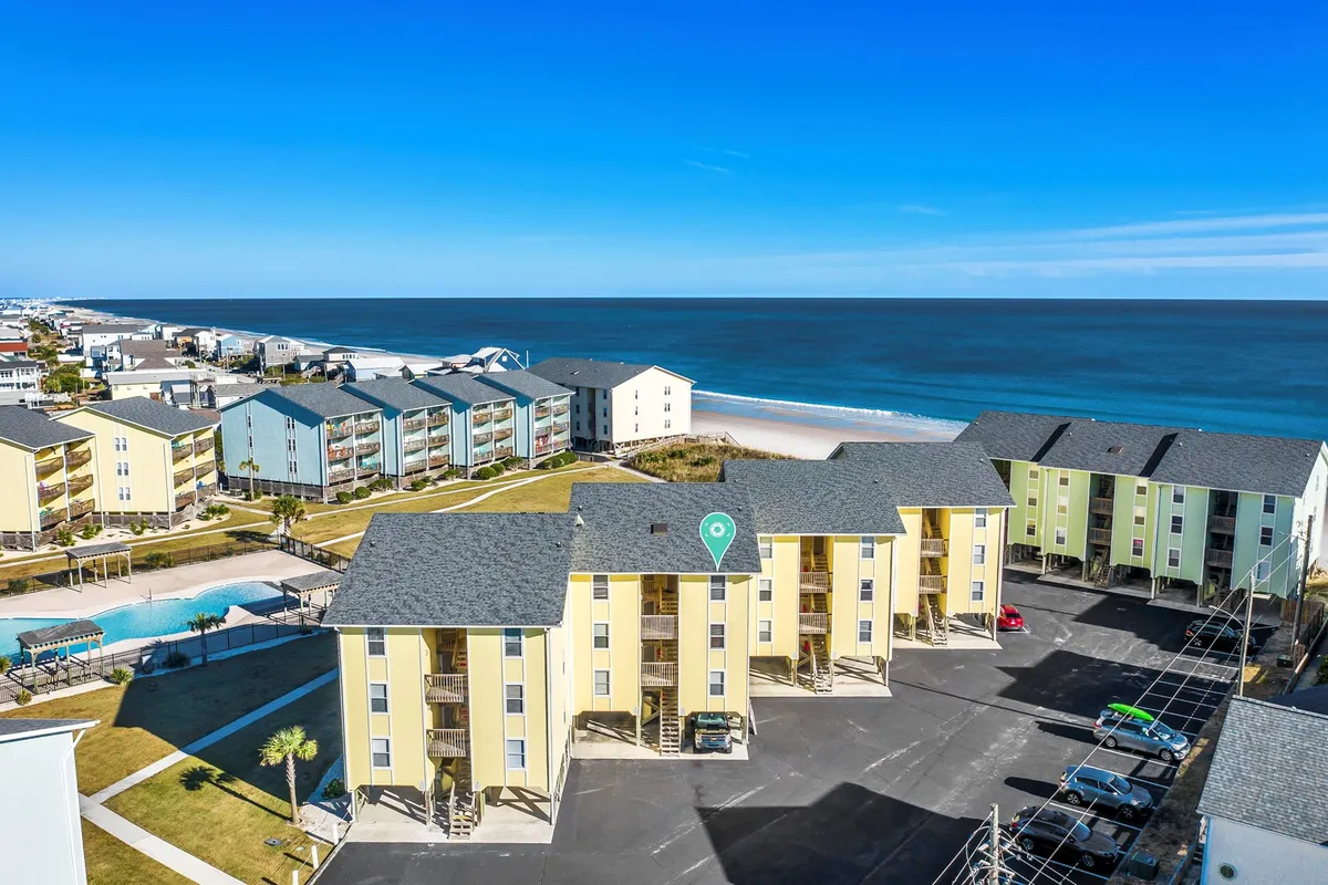 A colorful beachfront view featuring a swimming pool and vibrant buildings, with the ocean in the background. The pool area is inviting for both adults and children and highlights the amenities available for family enjoyment beyond the beach.