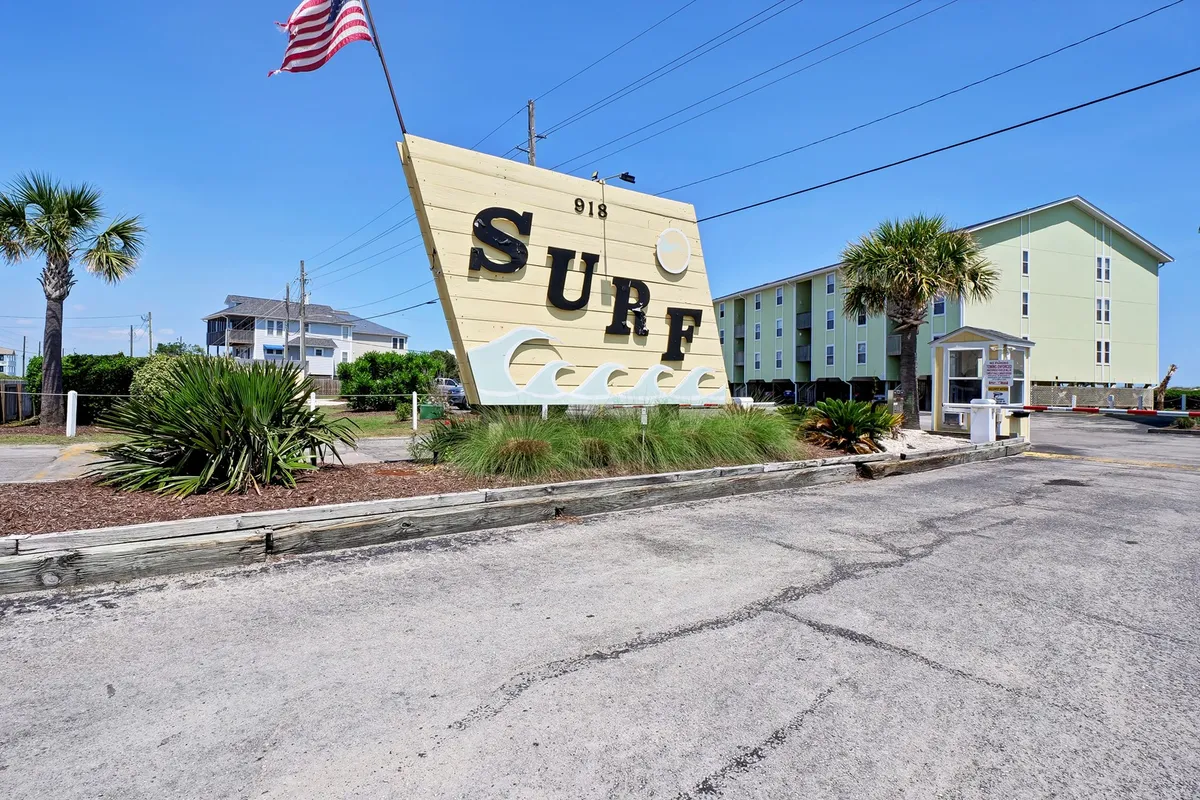 A vibrant exterior shot featuring a large 'SURF' sign, palm trees, and the building's facade, evoking a sense of arrival and the laid-back coastal lifestyle. The image hints at nearby beach access and local Surf City attractions.