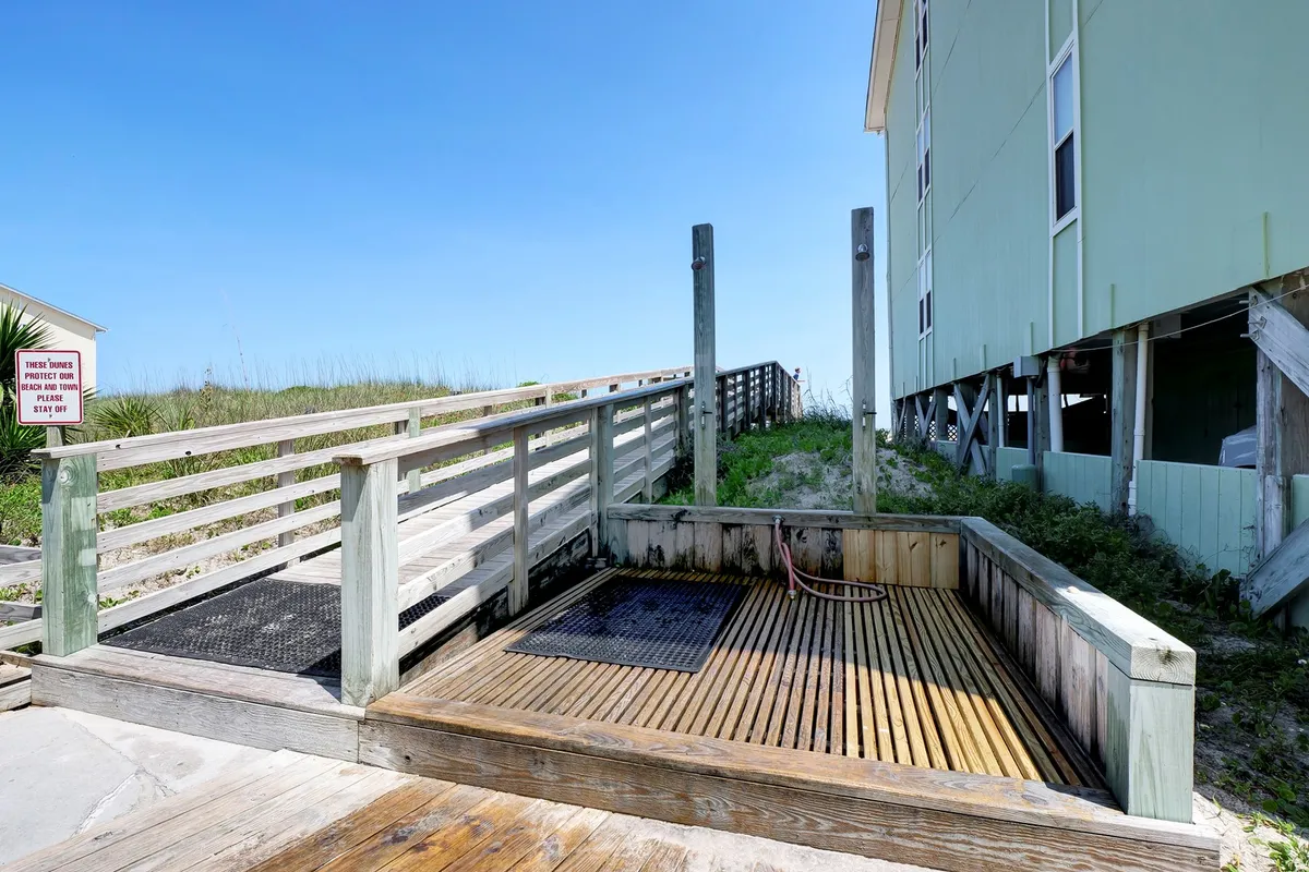 A wooden deck with a shower area, ramp, and lush greenery, conjuring the atmosphere of returning from the beach and enjoying outdoor moments. The deck offers a relaxed transition from beach to home, ideal for unwinding after a day’s adventure.