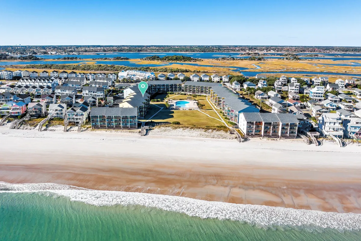 A stunning view of the beachfront with the swimming pool in the foreground, surrounded by homes and open green space. The image captures both ocean and poolside settings, suggesting opportunities for relaxation, group gatherings, and sunset views.